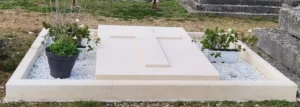 Monument funéraire en pierre claire avec une croix gravée et des gravillons blancs dans un cimetière
