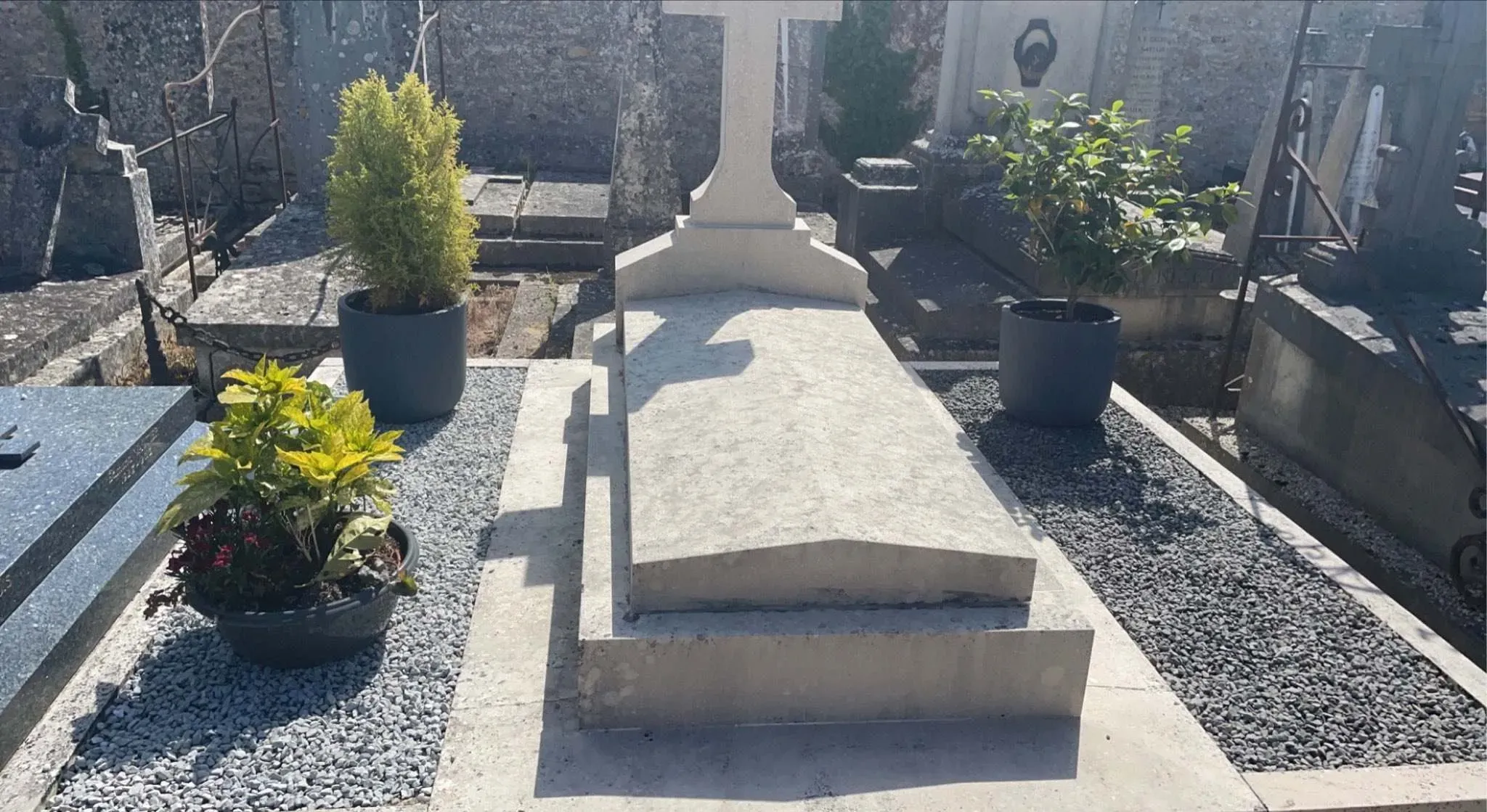 Monument funéraire classique rénové avec des gravillons et des plantes en pot.