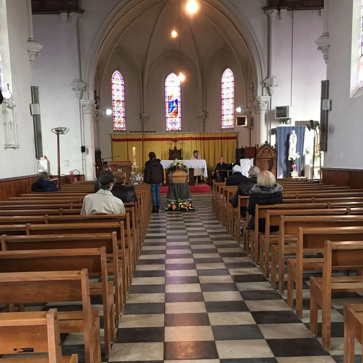 Cérémonie d'obsèques religieuse dans une église avec cercueil au centre.