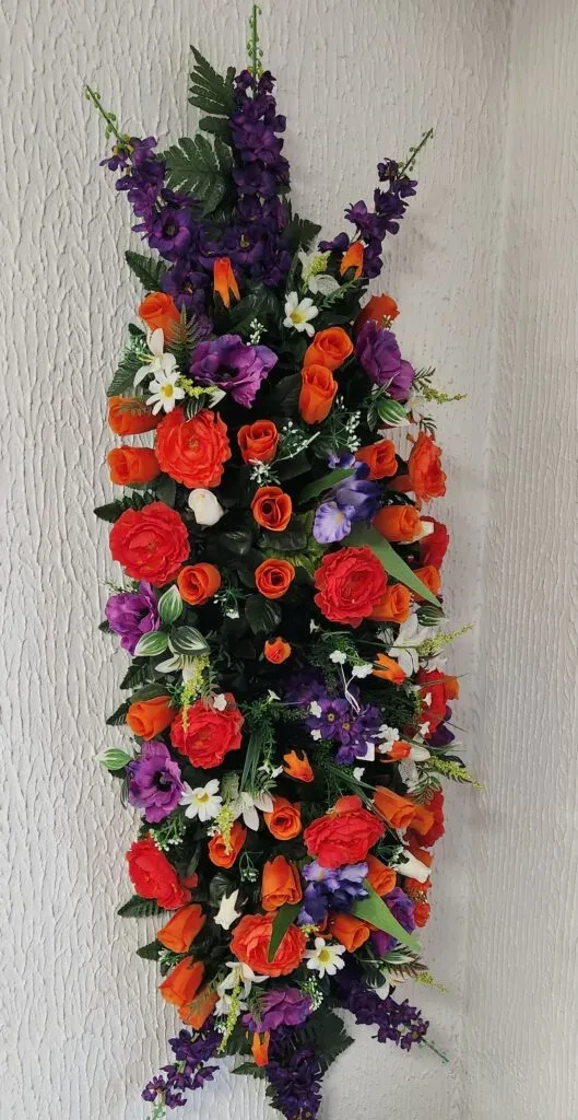 Dessus de cercueil en fleurs artificielles orange et violettes.
