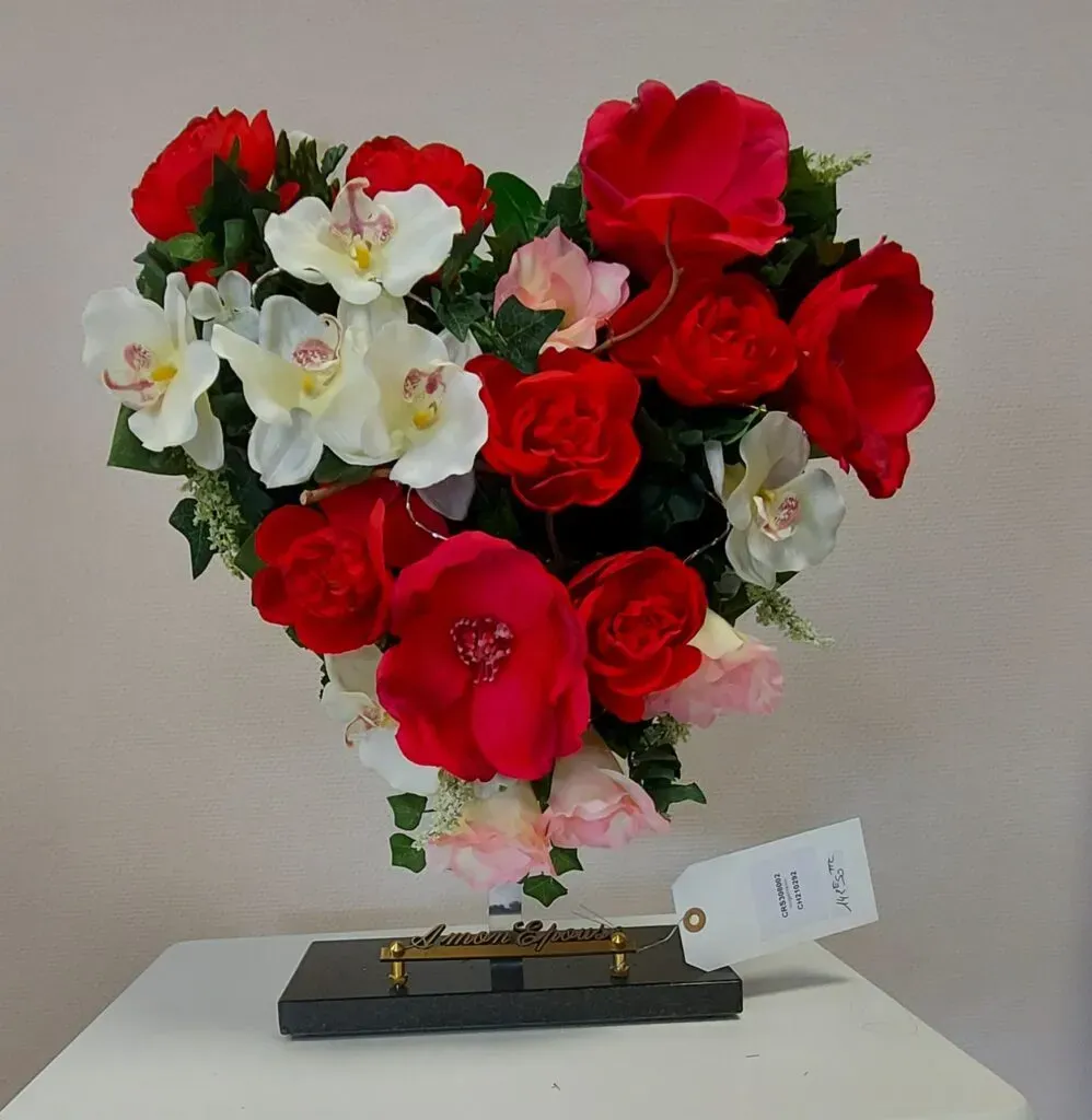 Cœur funéraire en fleurs artificielles rouges et blanches sur socle.