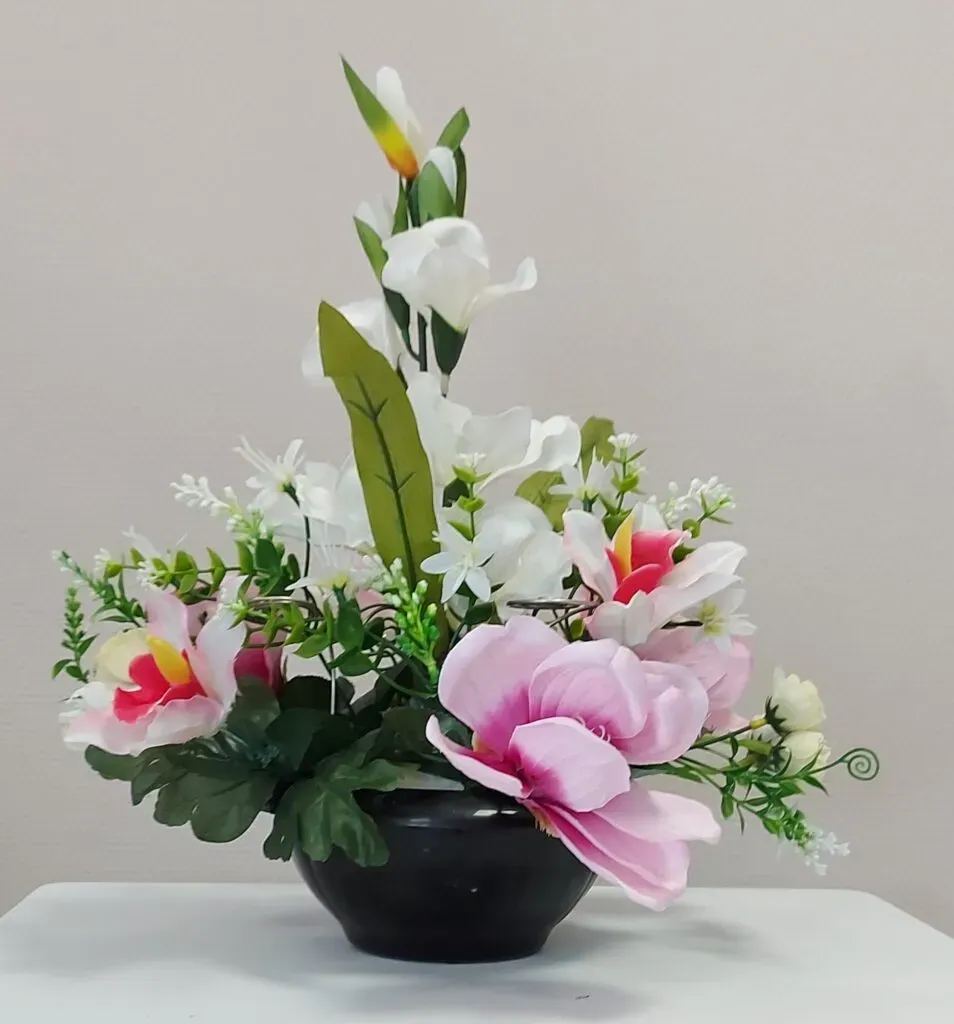 Composition de fleurs artificielles blanches et roses dans un pot noir.