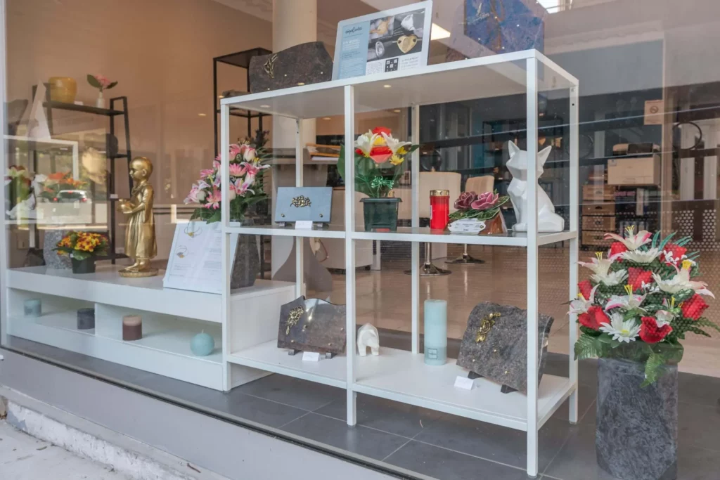 Vitrine de pompes funèbres avec plaques, fleurs artificielles et bougies.