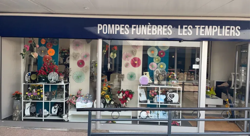 Vitrine de l'agence de pompes funèbres Les Templiers exposant des plaques et compositions florales