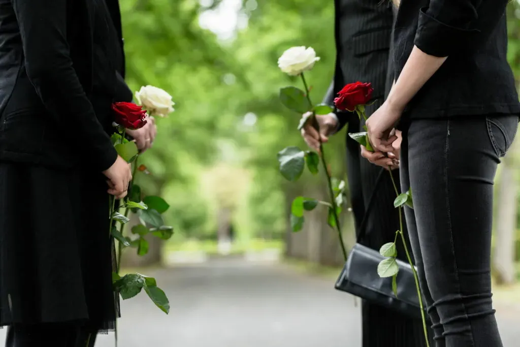 Proches tenant des roses rouges et blanches lors d'une cérémonie de funérailles.