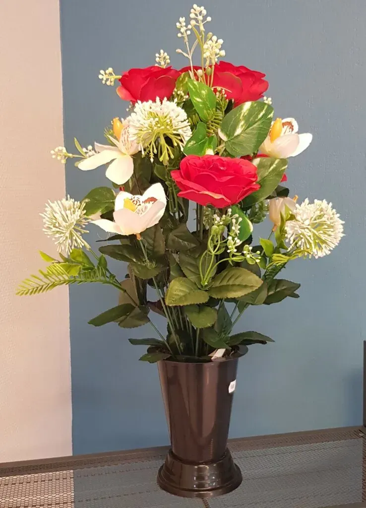 Bouquet de fleurs artificielles rouges et blanches dans un vase funéraire noir.
