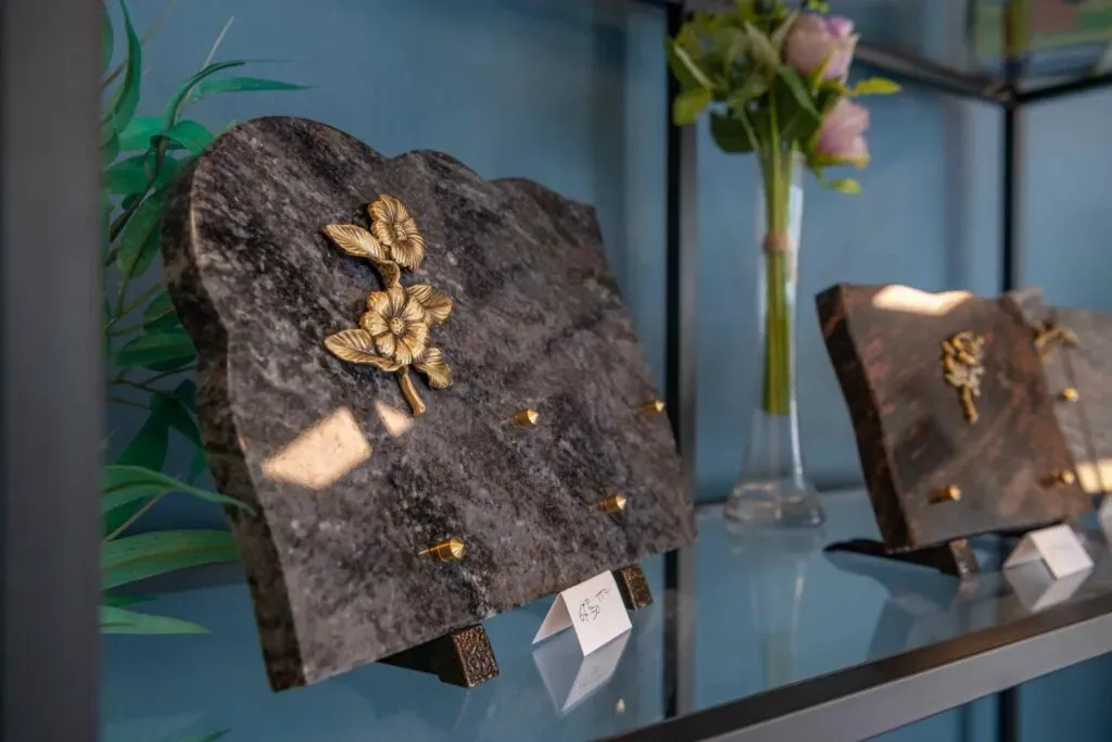 Plaque funéraire en granit gris gravée d'une fleur dorée exposée sur une étagère