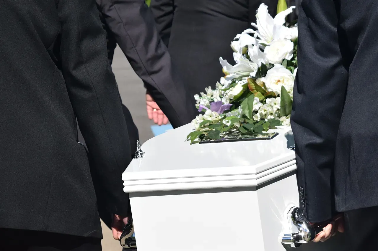 Porteurs en costume sombre transportant un cercueil blanc orné de fleurs.